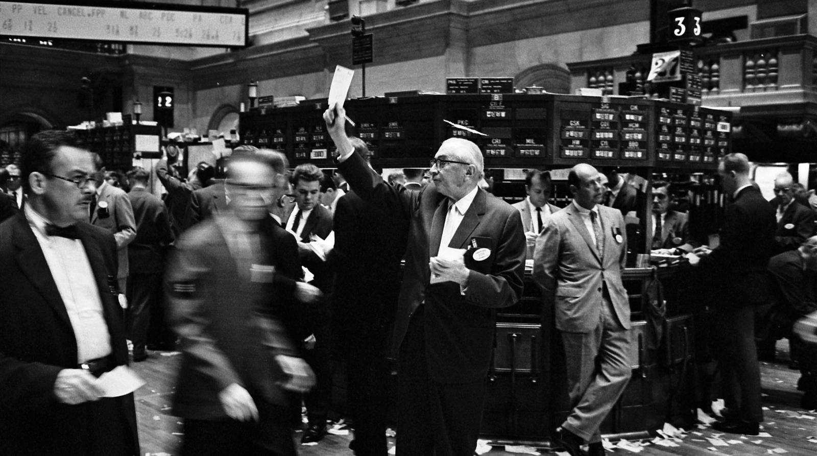 Le parquet du New York Stock Exchange en 1963, un courtier levant un ordre au milieu des postes de cotation, photographie en noir et blanc