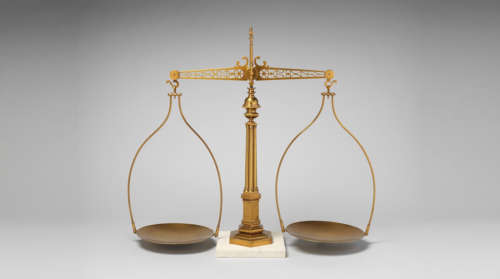Une balance à deux plateaux en laiton, le fléau à l'horizontale, sur un fond gris