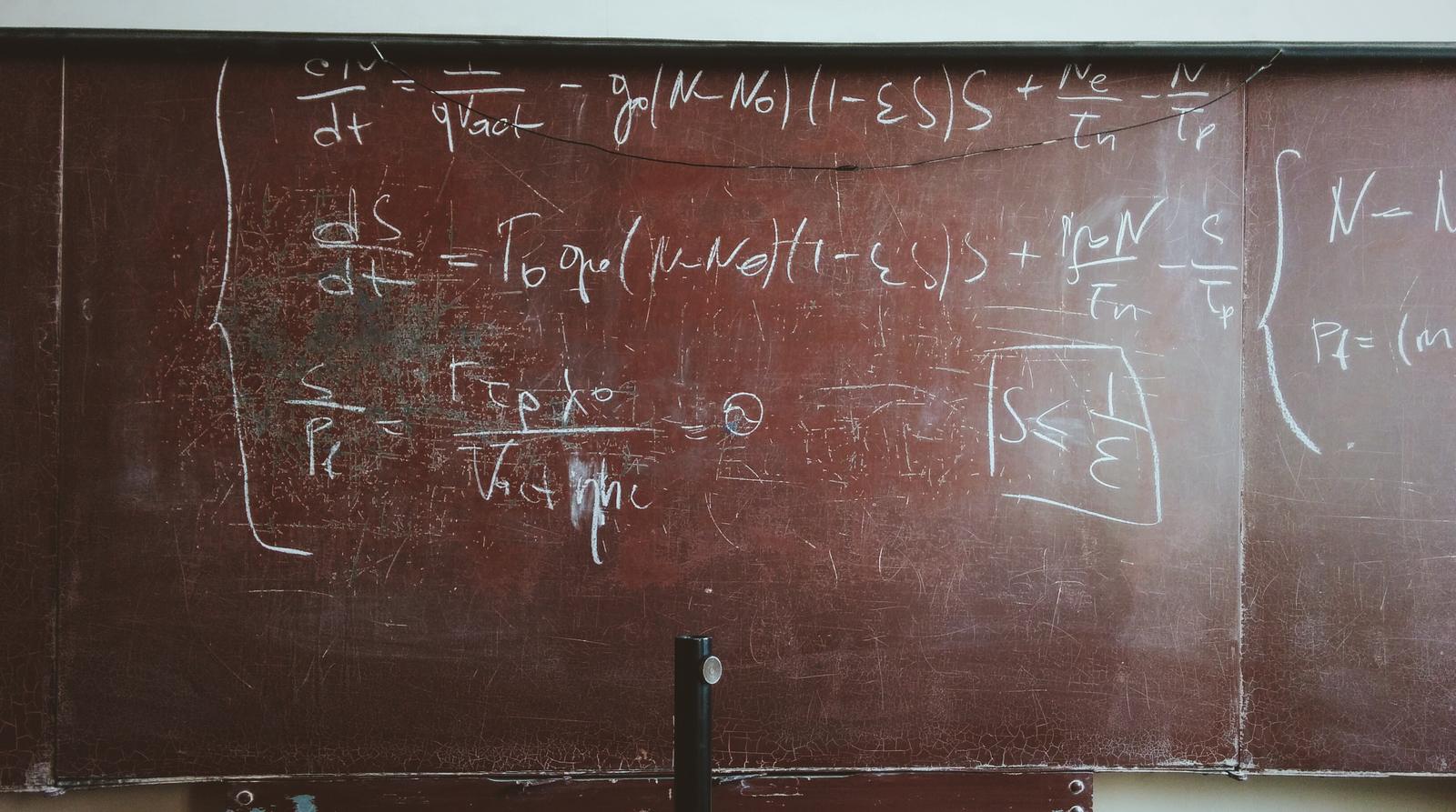 Un vieux tableau noir couvert de formules tracées à la craie, où se mêlent des lettres grecques