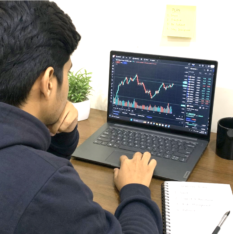Un trader qui étudie un graphique, un plan écrit au mur et un journal ouvert sur le bureau.